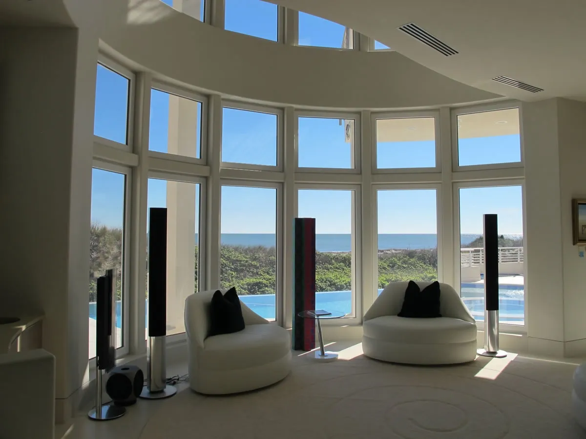 Curved wall of tall windows looking out over a pool and the ocean from a living room